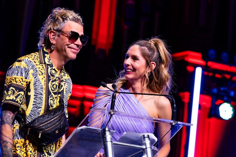 Two presenters at a podium during the 2026 AIR Awards, one wearing a patterned shirt and sunglasses, looking smilingly at a woman in a purple dress.